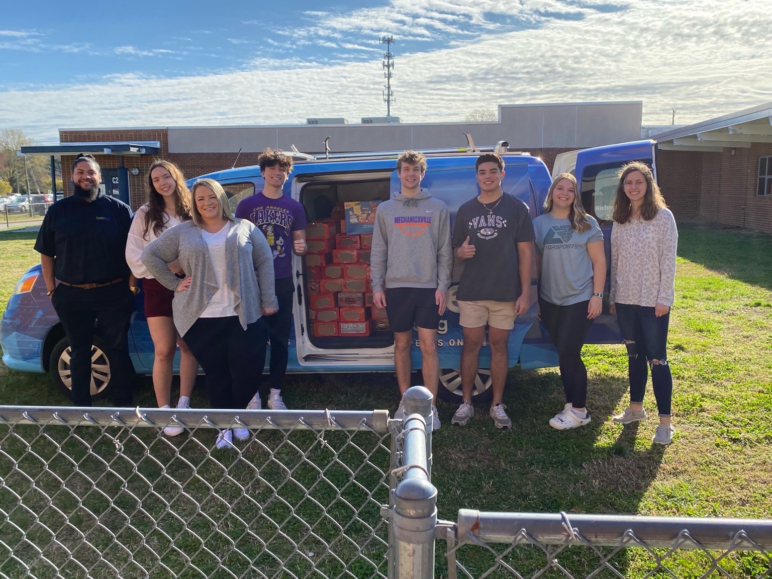Two CodeBlue employees and several Mechanicsville High School students posed in front of van full of donated food items.